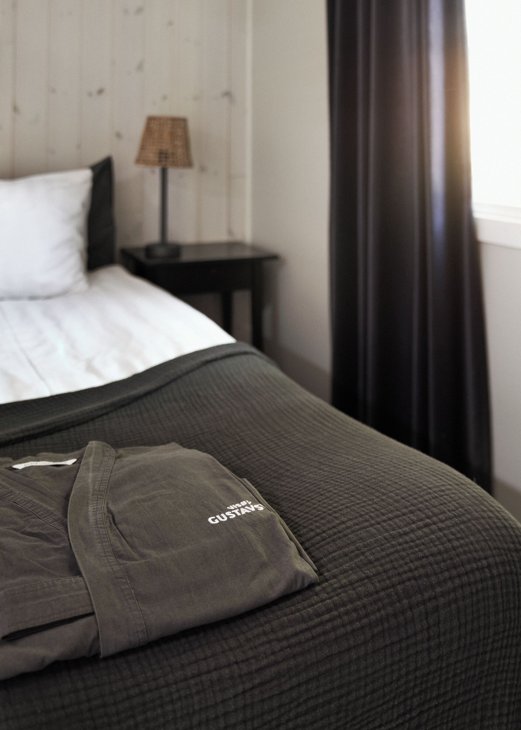 A neatly made bed with a pillow and a folded shirt on it.