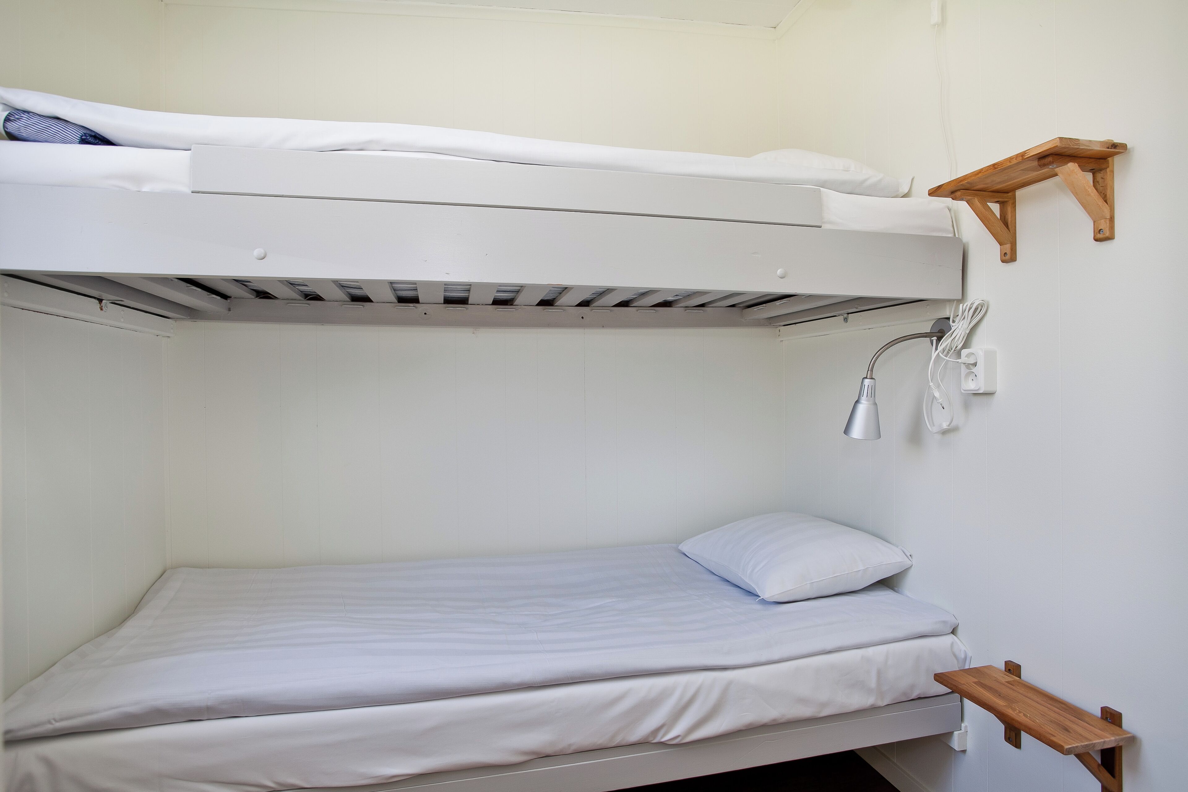 Una cama litera con un estante de madera fijado a la pared superior.