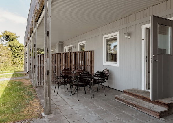 A covered patio with a table and chairs, a wooden fence, and a door leading to the interior. - Visby Gustavsvik (Visby)