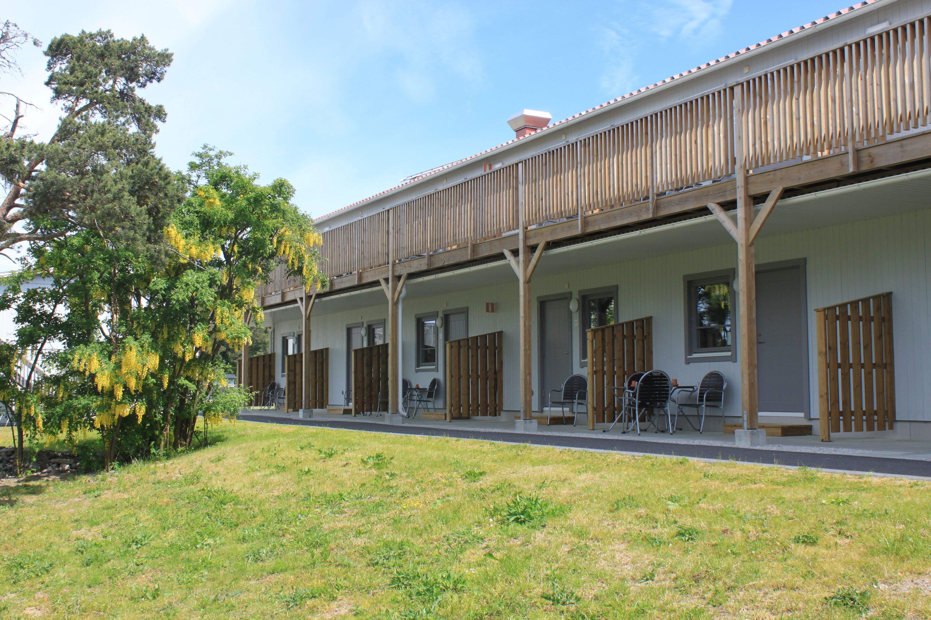 Een gebouw met twee verdiepingen, een overdekt terras, zitplaatsen buiten en een gazon.
