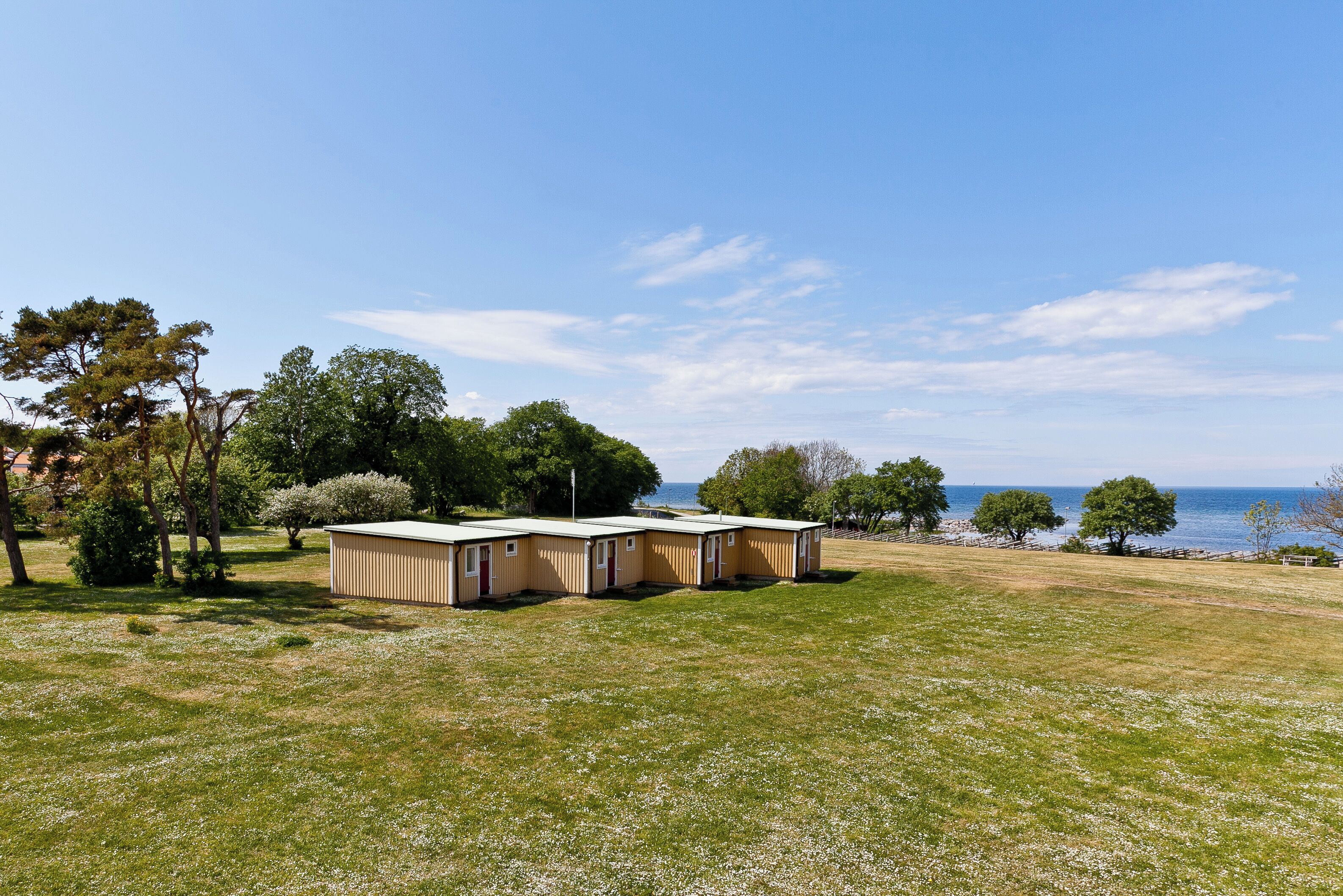 A row of mobile homes with a grassy field and trees in the background.