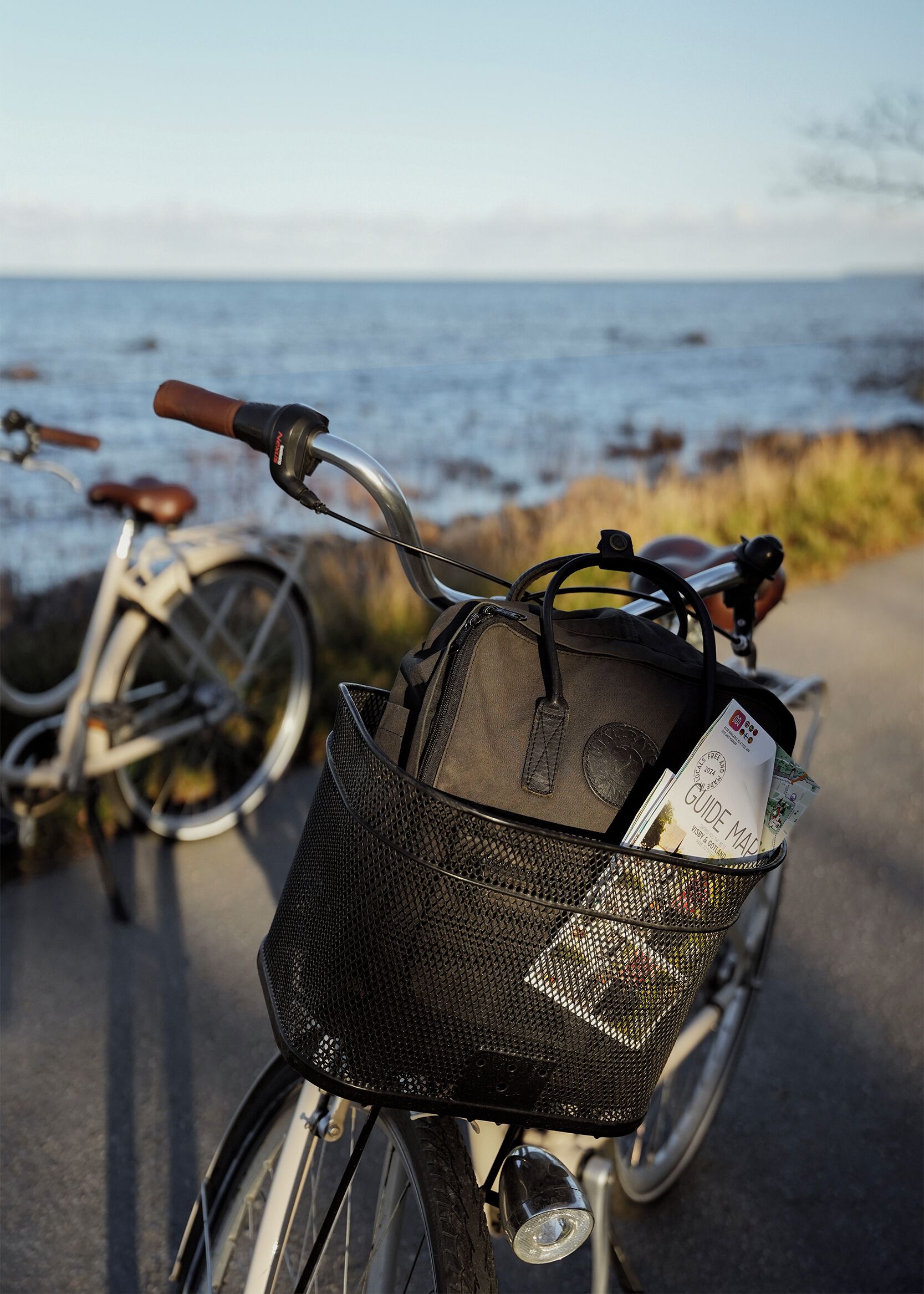 Een fiets met een mand waarin een kaart en een tas zitten, geparkeerd bij een waterpartij.