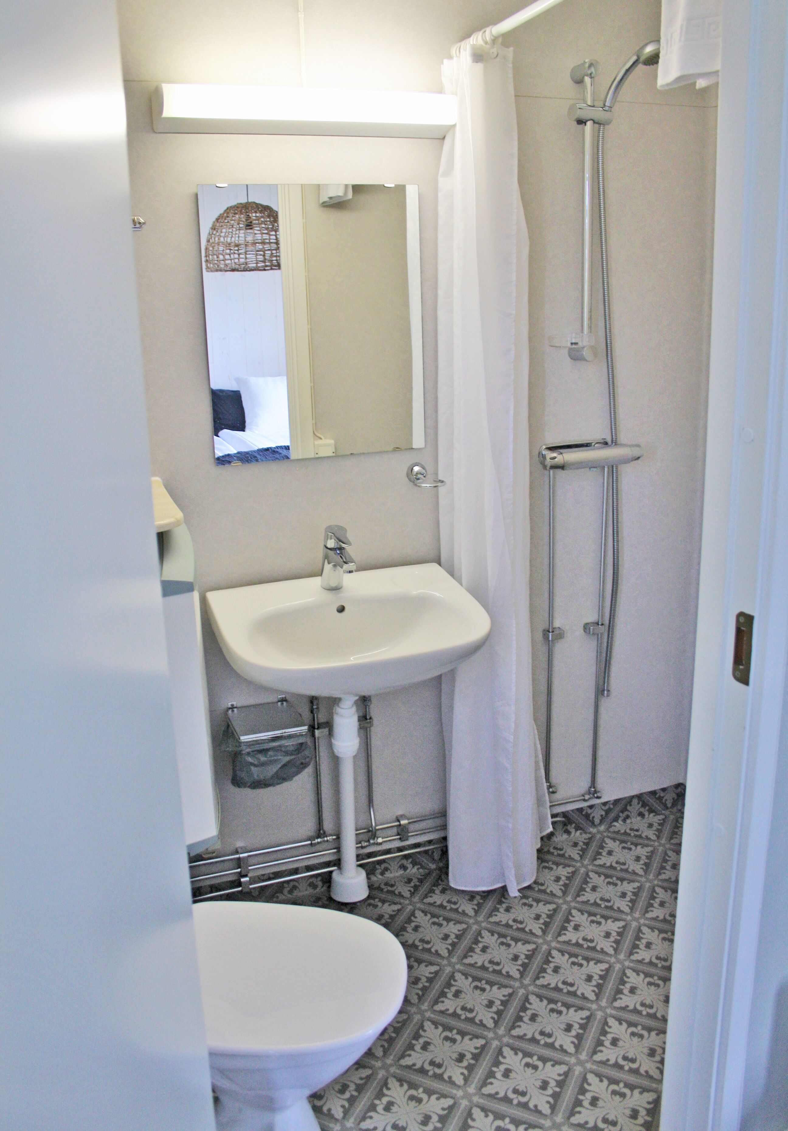A bathroom with a sink, mirror, shower, and patterned floor tiles.