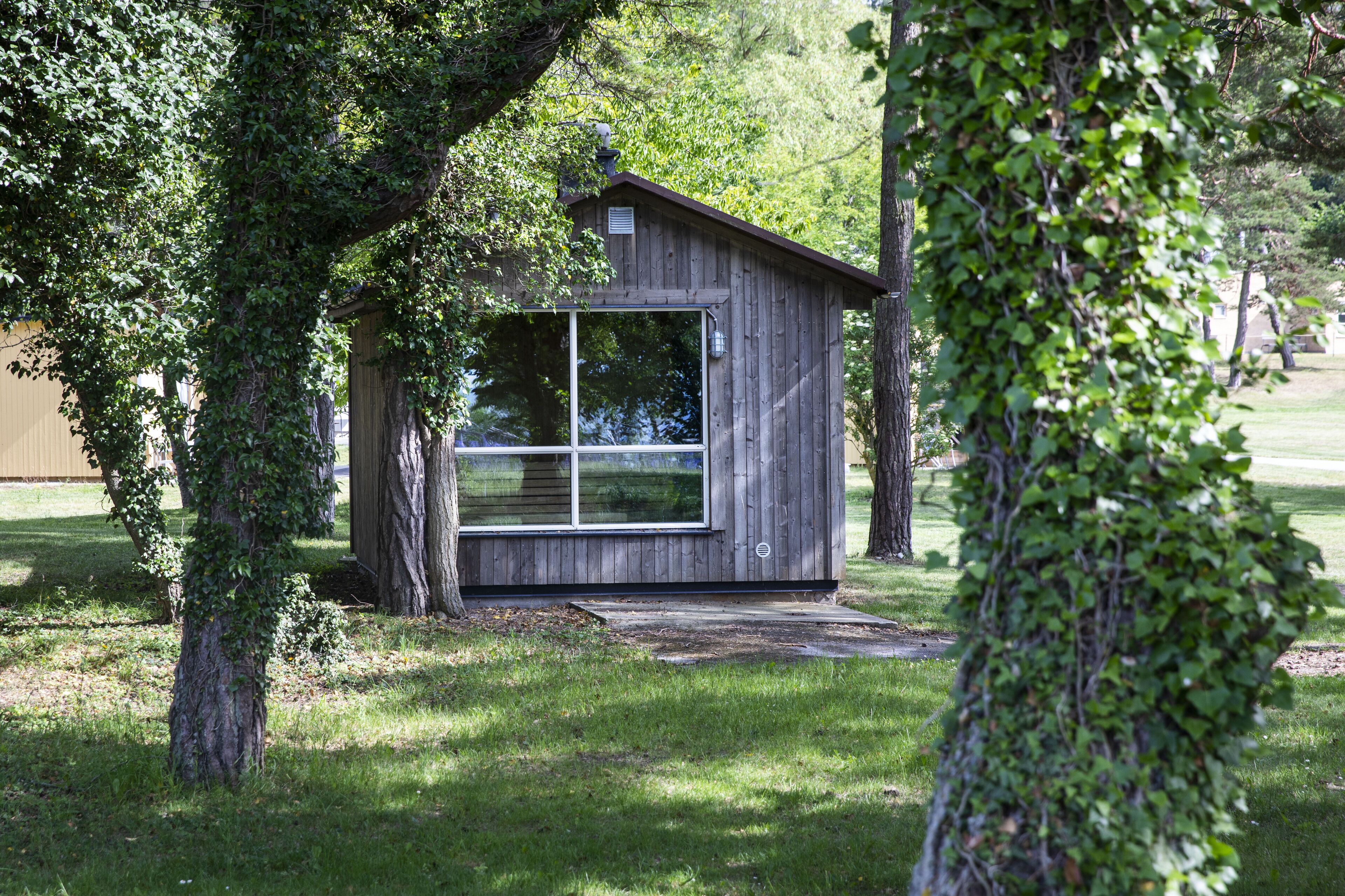 A small wooden cabin with a large window, surrounded by trees and grass.