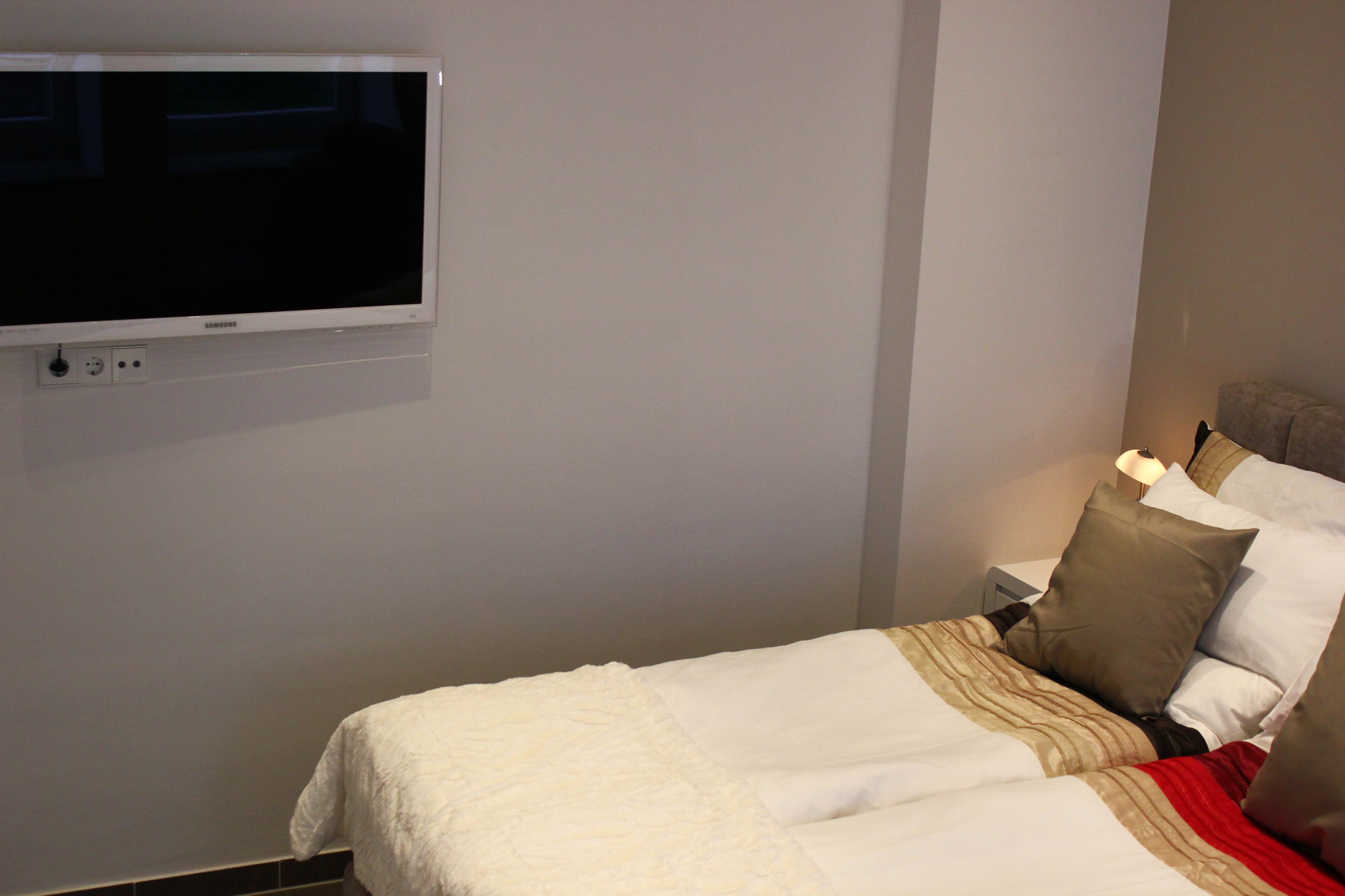 A hotel room with a bed, pillows, a bedside table, and a TV mounted on the wall.