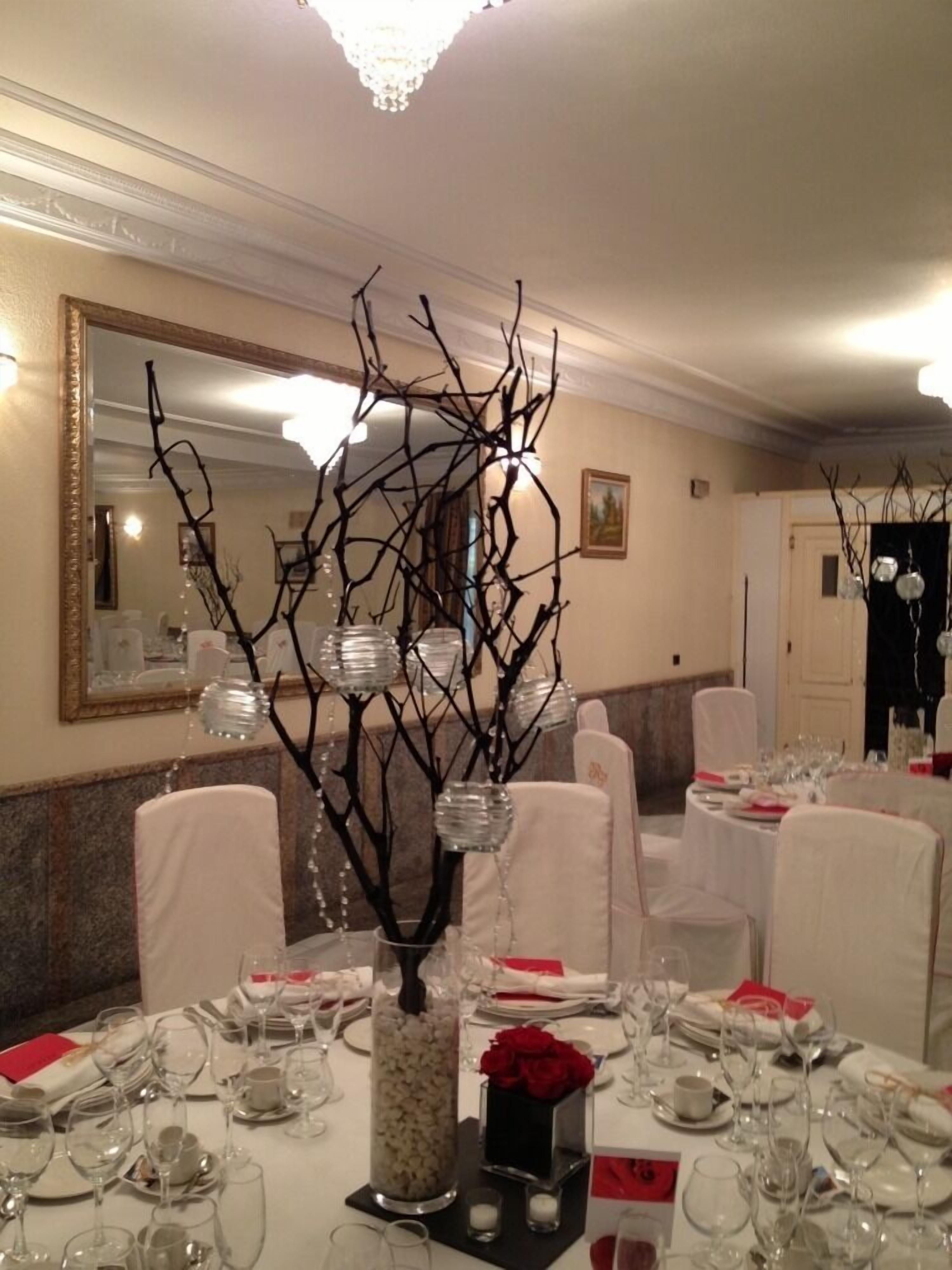 Een balzaal met ronde tafels gedekt voor een formeel evenement, met een centraal decoratief arrangement van takken en glazen vazen.