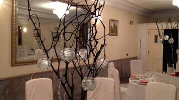 Een balzaal met ronde tafels gedekt voor een formeel evenement, met een centraal decoratief arrangement van takken en glazen vazen.