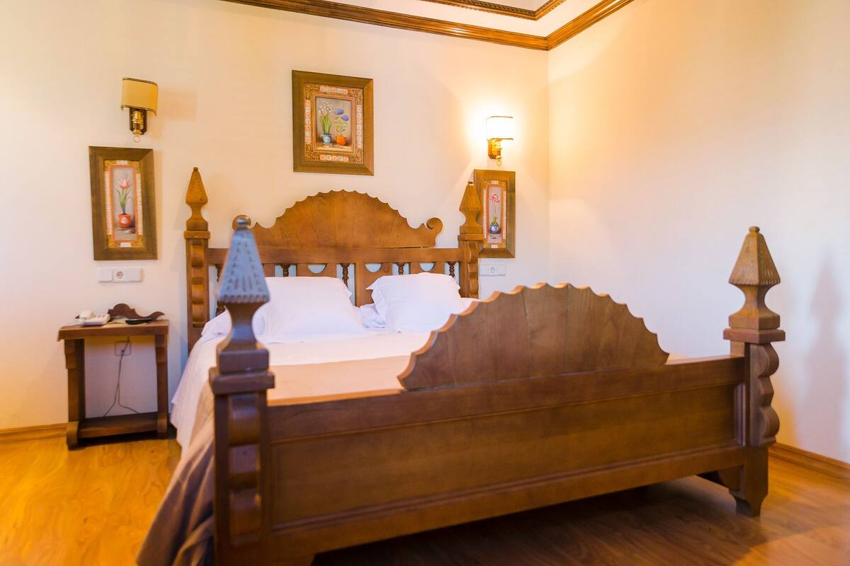 Ein hölzernes Himmelbett mit weißen Leinen, ein Nachttisch mit Lampe und gerahmte Kunstwerke an den Wänden.