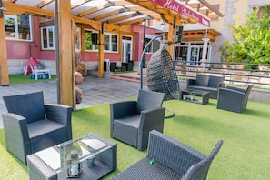 En utomhusplats med sittmöbler i rotting och ett bord i glas, en hängstol och en skylt för ”Hotel Paladium Bonner”.
