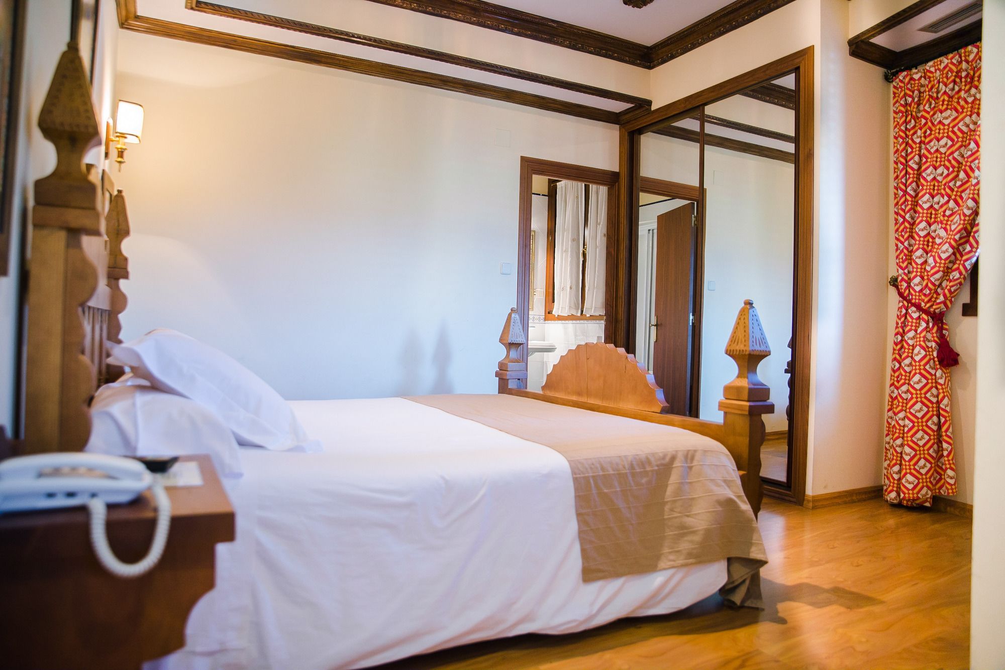 Una habitación de hotel con cama, mesita de noche, lámpara y espejo.
