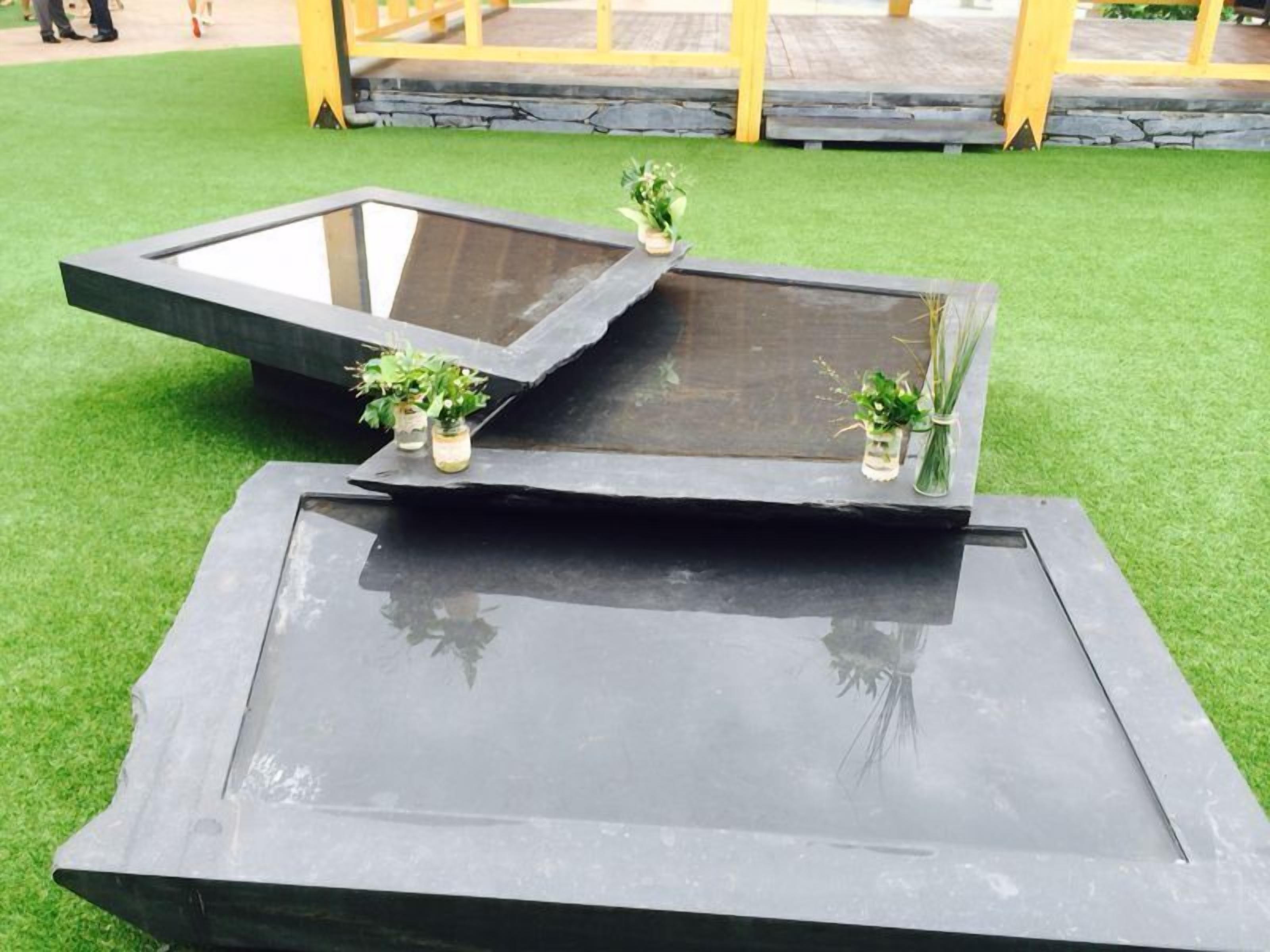 A modern outdoor seating area with a rectangular table and two square tables, each with a glass top. There are small potted plants on the tables.