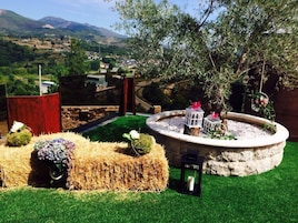 Un jardín con un macetero de piedra circular, fardos de heno y un pequeño árbol.