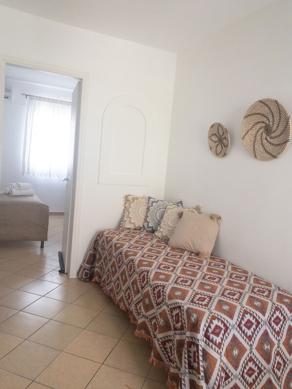 A bedroom with a bed, patterned bedding, a door, and a view into another room. - Aloni Ios (Ios)