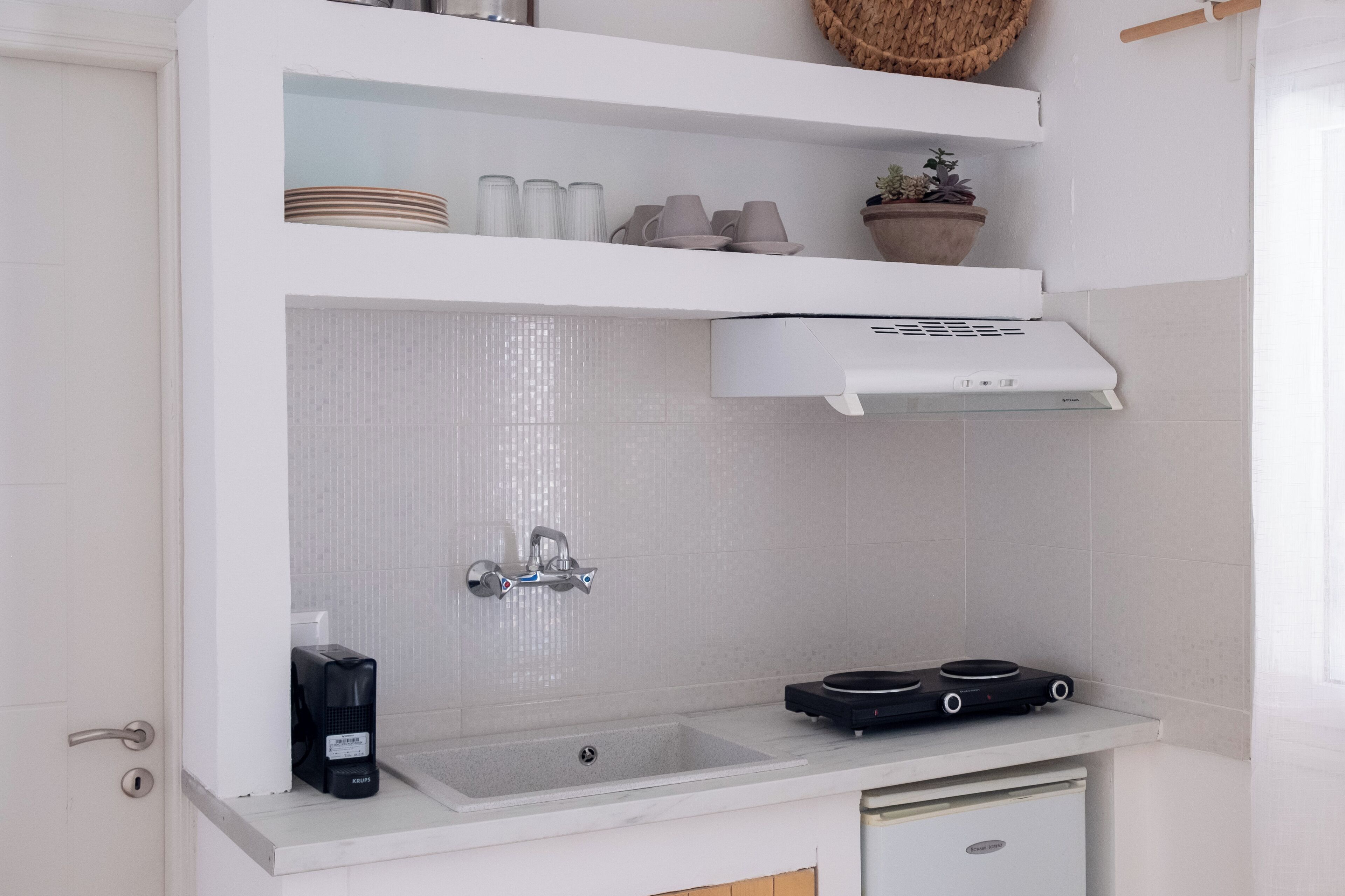 A compact kitchen with a built-in sink, a coffee maker, and a small stove.