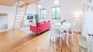 A modern living space with a wooden floor, a pink sofa, a dining table with chairs, a TV, and a staircase. - Look At Me - Serviced Lofts & Studios (Porto)