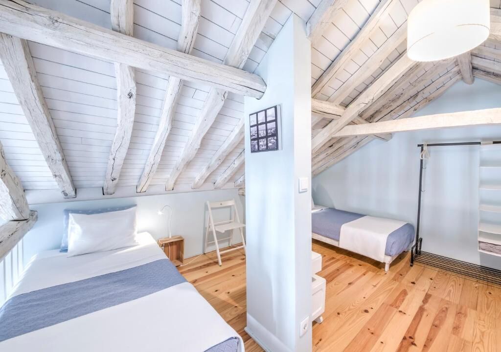 Un dormitorio con una cama grande, una cama más pequeña, vigas de madera, una escalera y una ventana.