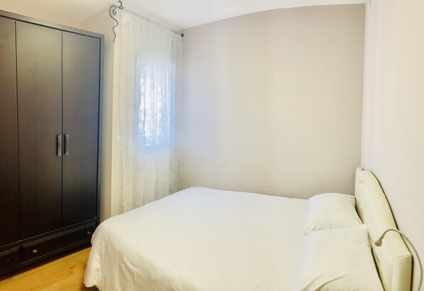 A bedroom with a bed, a wardrobe, and a window with curtains. - Royal Apartments (Netanya)