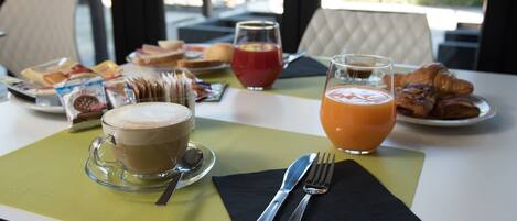 Una mesa de desayuno con una taza de café, croissants, jugo de naranja y diversas bollerías.
