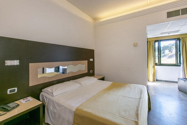 Une chambre d’hôtel avec un lit, une table de chevet et un miroir. Il y a une fenêtre avec des rideaux et une vue sur l’extérieur.