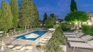 A swimming pool with lounge chairs and umbrellas, surrounded by trees and a fence.