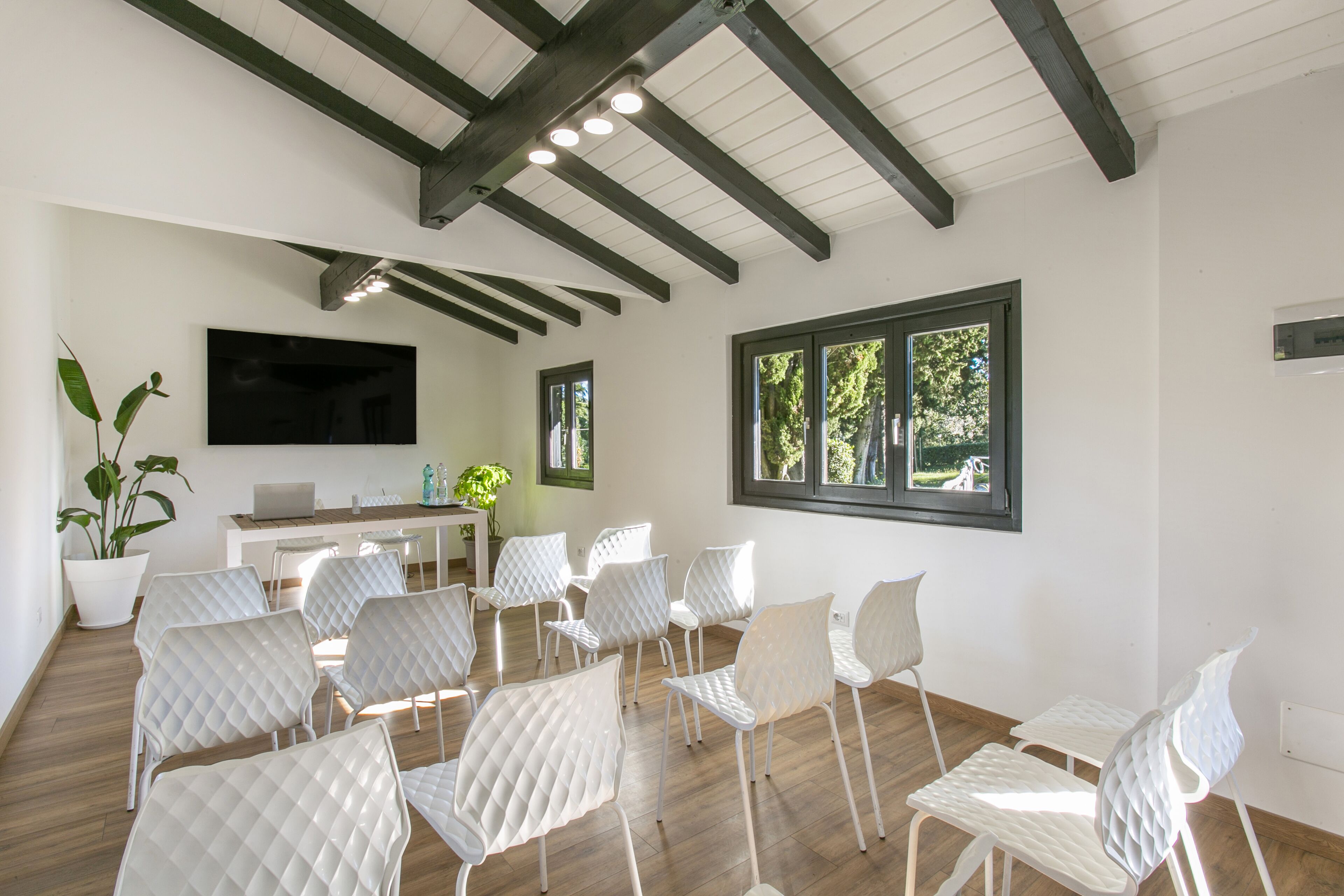 A conference room with white chairs, a desk with a laptop, a TV, and large windows.
