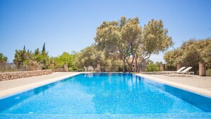 A rectangular swimming pool with clear blue water, surrounded by a stone wall and trees. - Agroturismo Son Not (Arta)