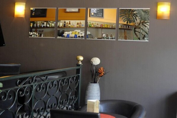 A bar area with a counter, shelves with bottles, and a decorative mirror with a plant. - Hôtel Le Ceïtya (Saint-Gilles-Croix-de-Vie)