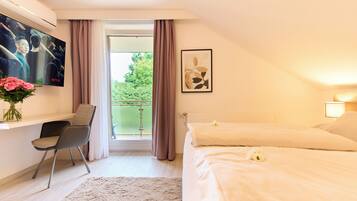 A hotel room with a bed, a desk with a chair, a TV mounted on the wall, and a window with curtains.