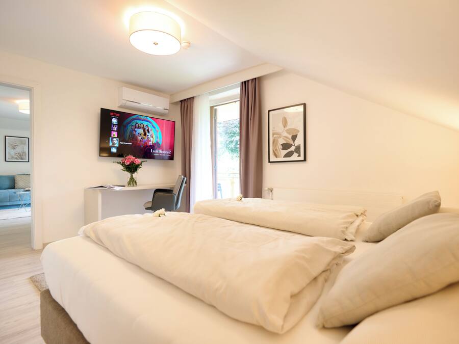 Habitación de hotel con una cama grande, un escritorio con computadora, un televisor montado en la pared y una ventana con cortinas.