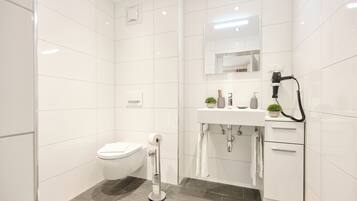 A modern bathroom with white tiles, a toilet, a sink with a mirror, a hairdryer, and a towel rack.