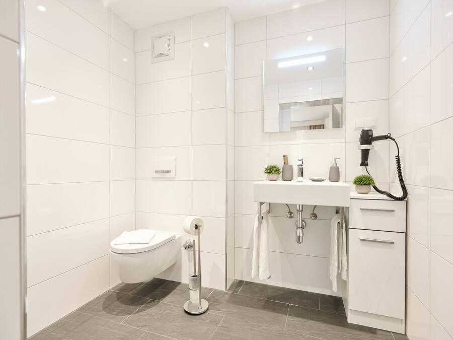 A modern bathroom with white tiles, a toilet, a sink with a mirror, a hairdryer, and a towel rack.