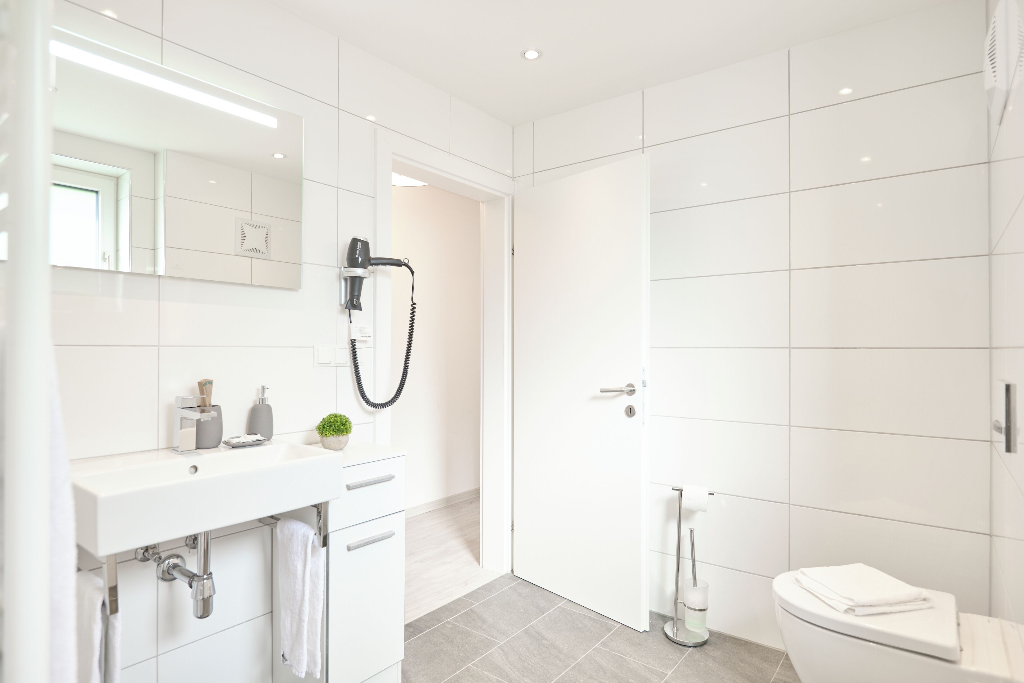 Ein modernes Badezimmer mit Waschbecken, Spiegel und Toilette in Weiß.