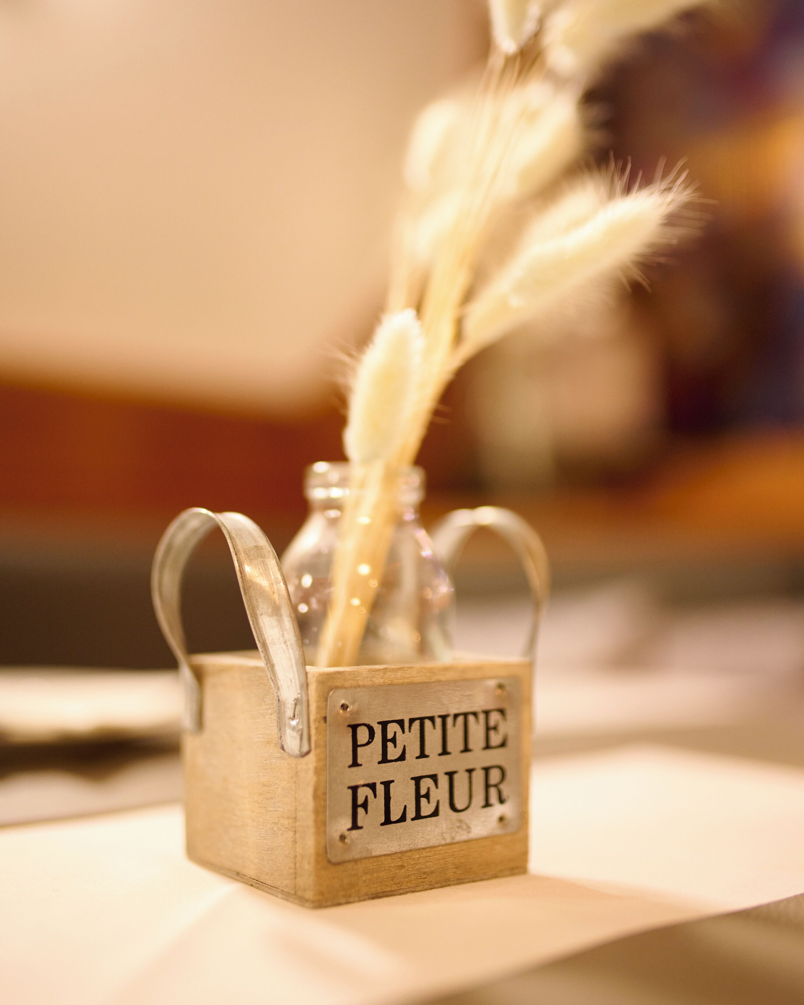 Een klein houten doosje met de aanduiding 'PETITE FLEUR' waarin een veer en een glazen pot zitten.