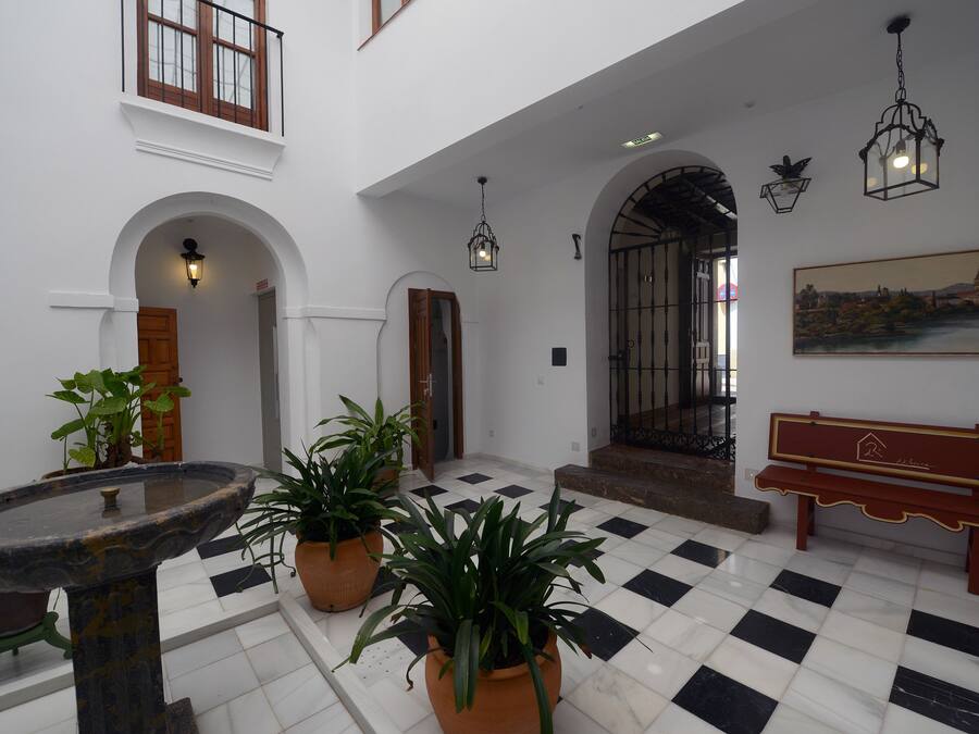 Un vestíbulo espacioso con piso a cuadros, una fuente, plantas en macetas, un banco y un cuadro en la pared.