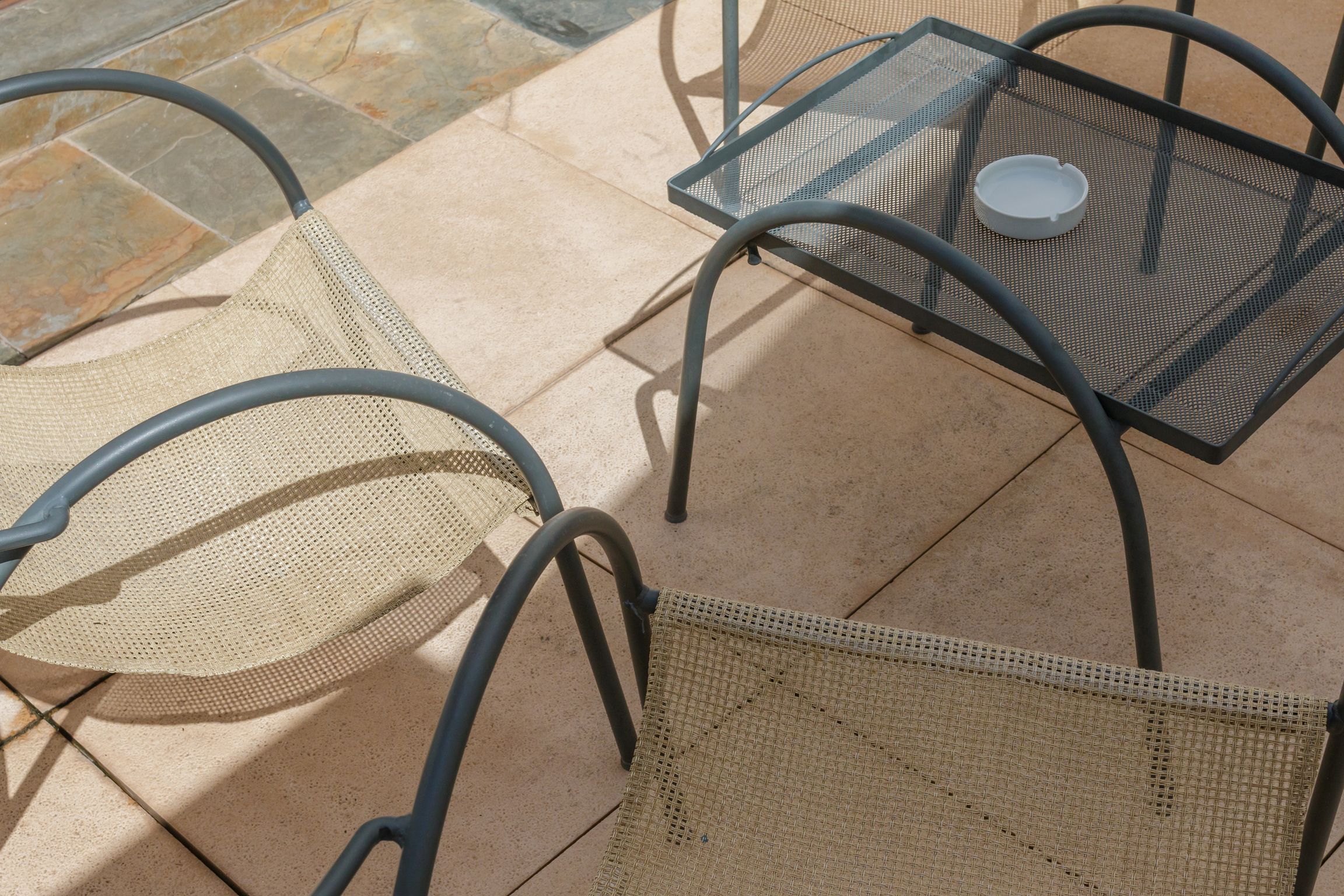 Un patio con sillas y una mesa de metal, con un cojín de asiento tejido y una bandeja de metal.
