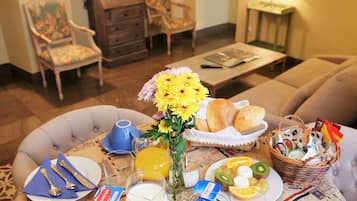 A breakfast setting with a table set for two, including plates, cutlery, a vase of flowers, a basket of bread, and various breakfast items.