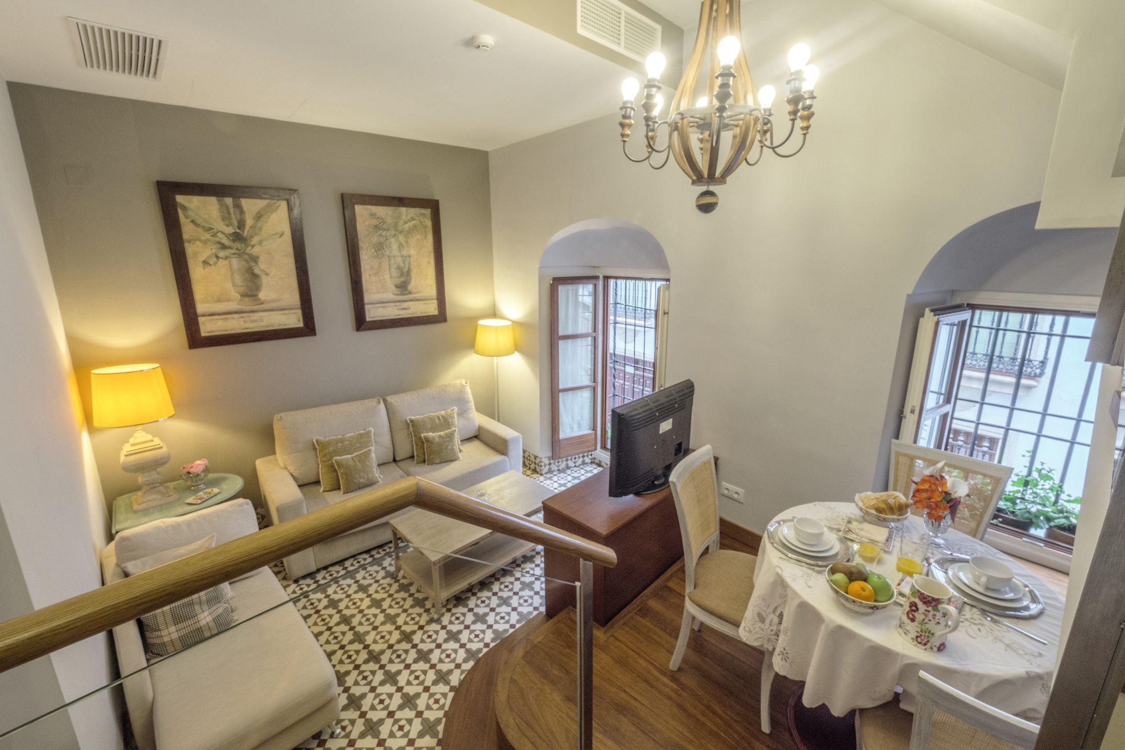 Una sala de estar moderna con un sofá, una mesa de comedor preparada para el desayuno y una escalera que conduce a otro nivel.