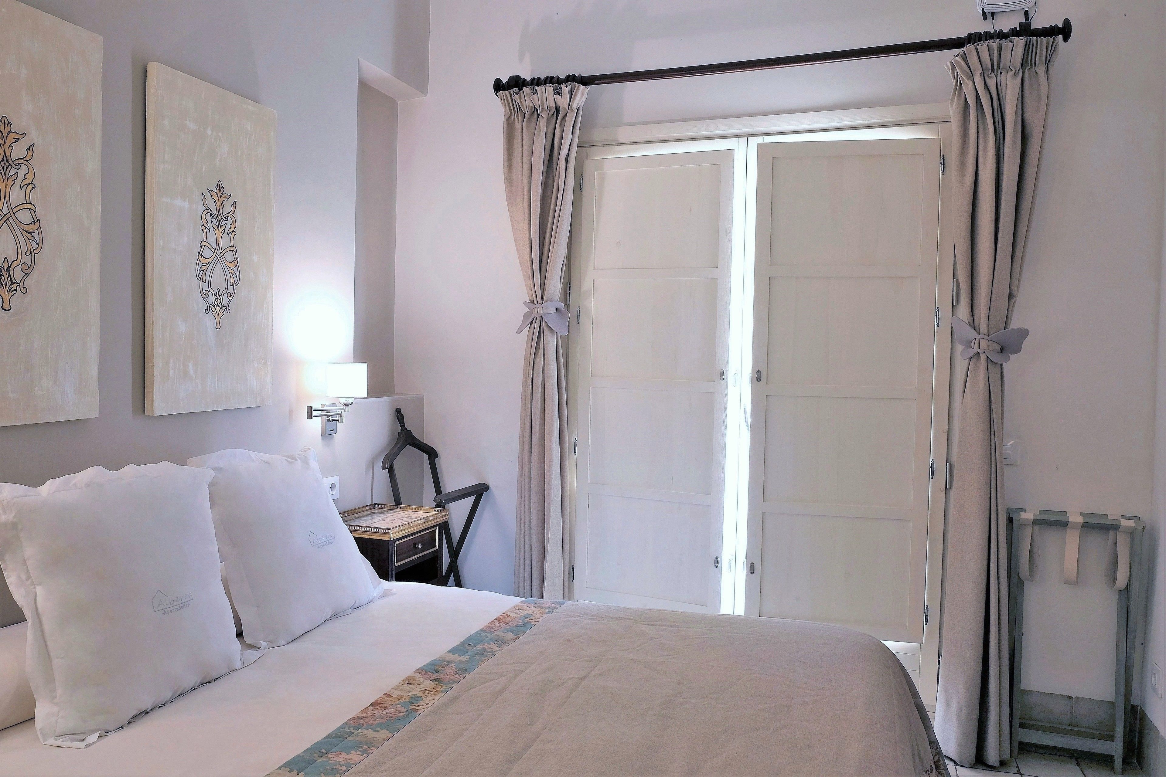 A bedroom with a bed, two pillows, a nightstand, a chair, and a door with curtains.