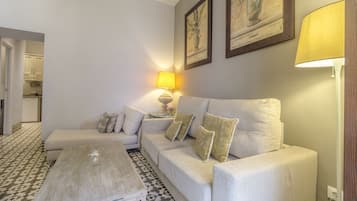 A living room with a sofa, a coffee table, and a lamp. There are framed pictures on the wall and a patterned floor.