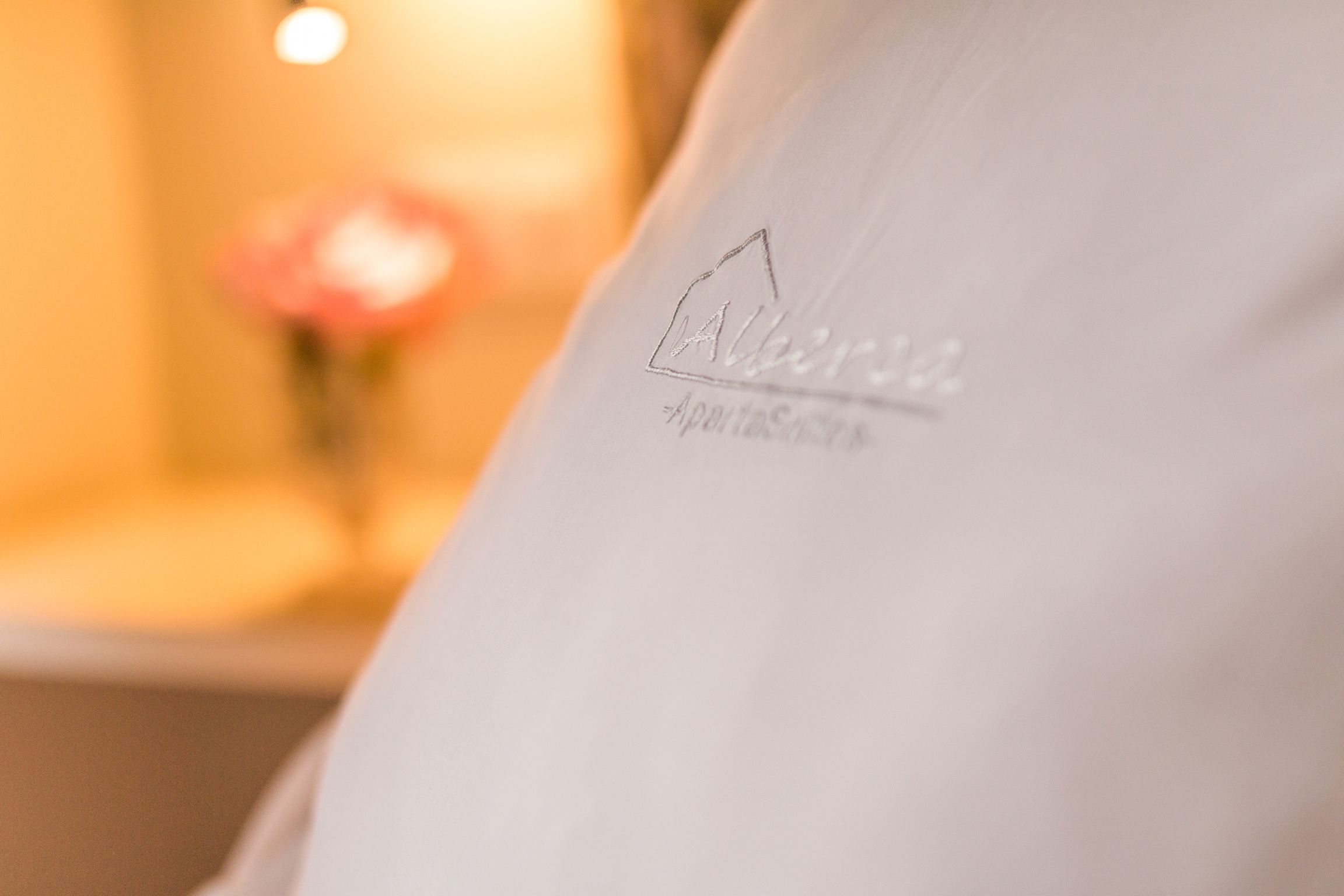 A close-up of a white pillow with the logo "Allure" and the text "Apostolios" on it.