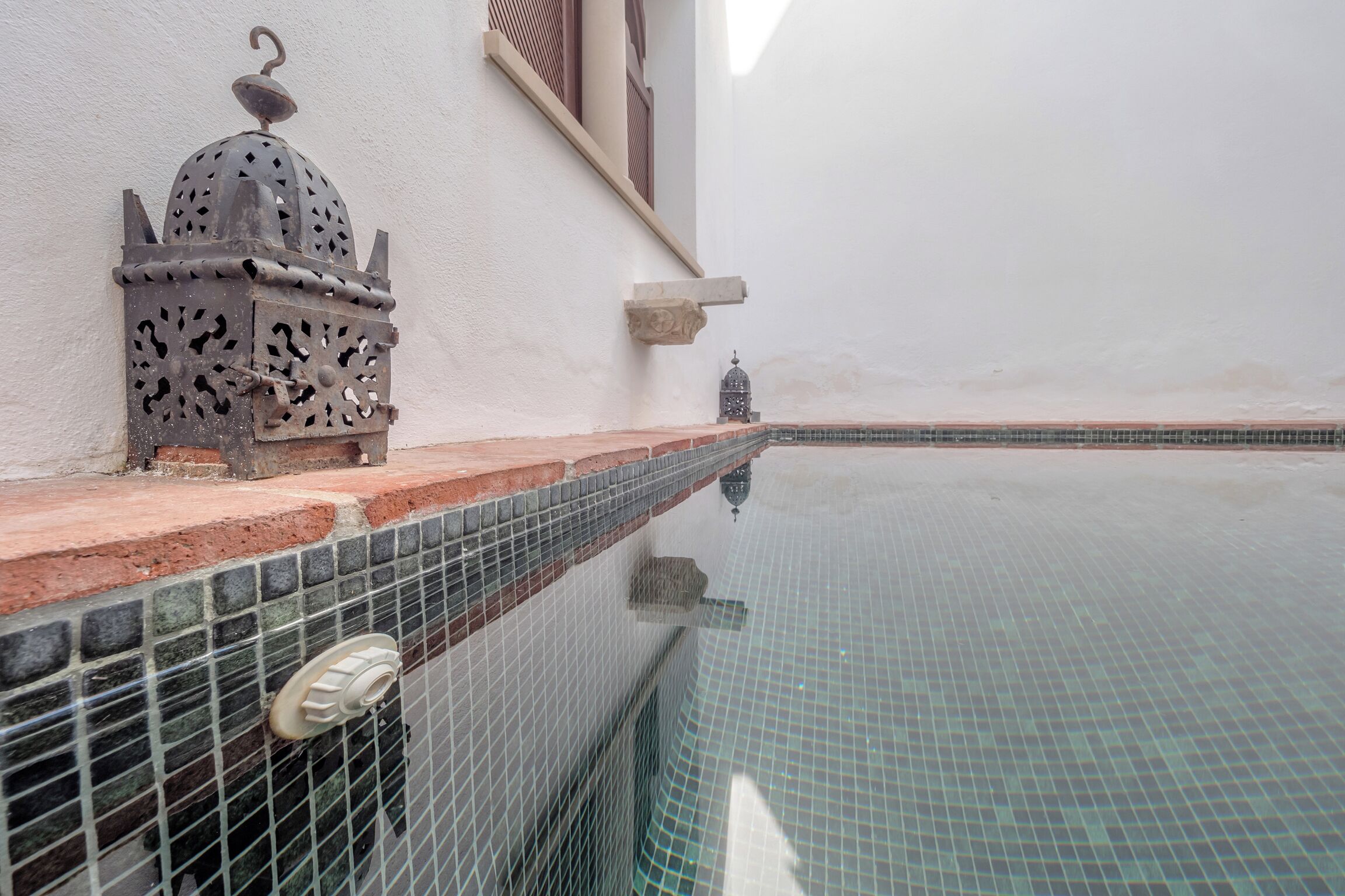 Ein Swimmingpool mit Fliesenrand, eine verzierte Metalllaterne und ein kleiner Vogelkäfig.