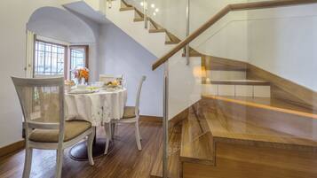 A dining area with a table set for four, a chair, and a staircase with wooden steps and glass railings.