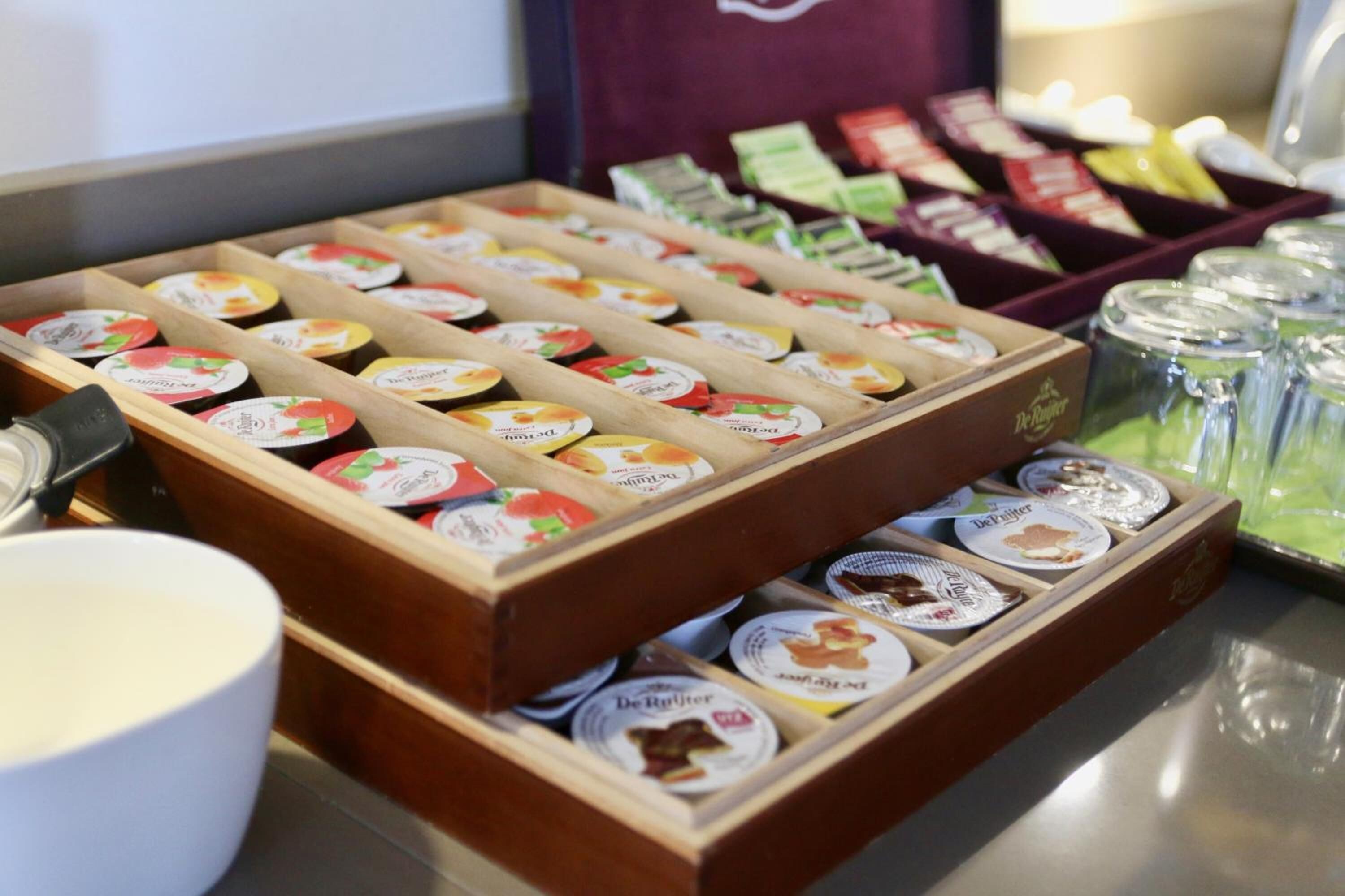 A display of packaged food items in wooden boxes with labels, a white bowl, and jars on a counter.