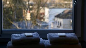 A window with two towels stacked on a windowsill, overlooking a cityscape with buildings and a tower.