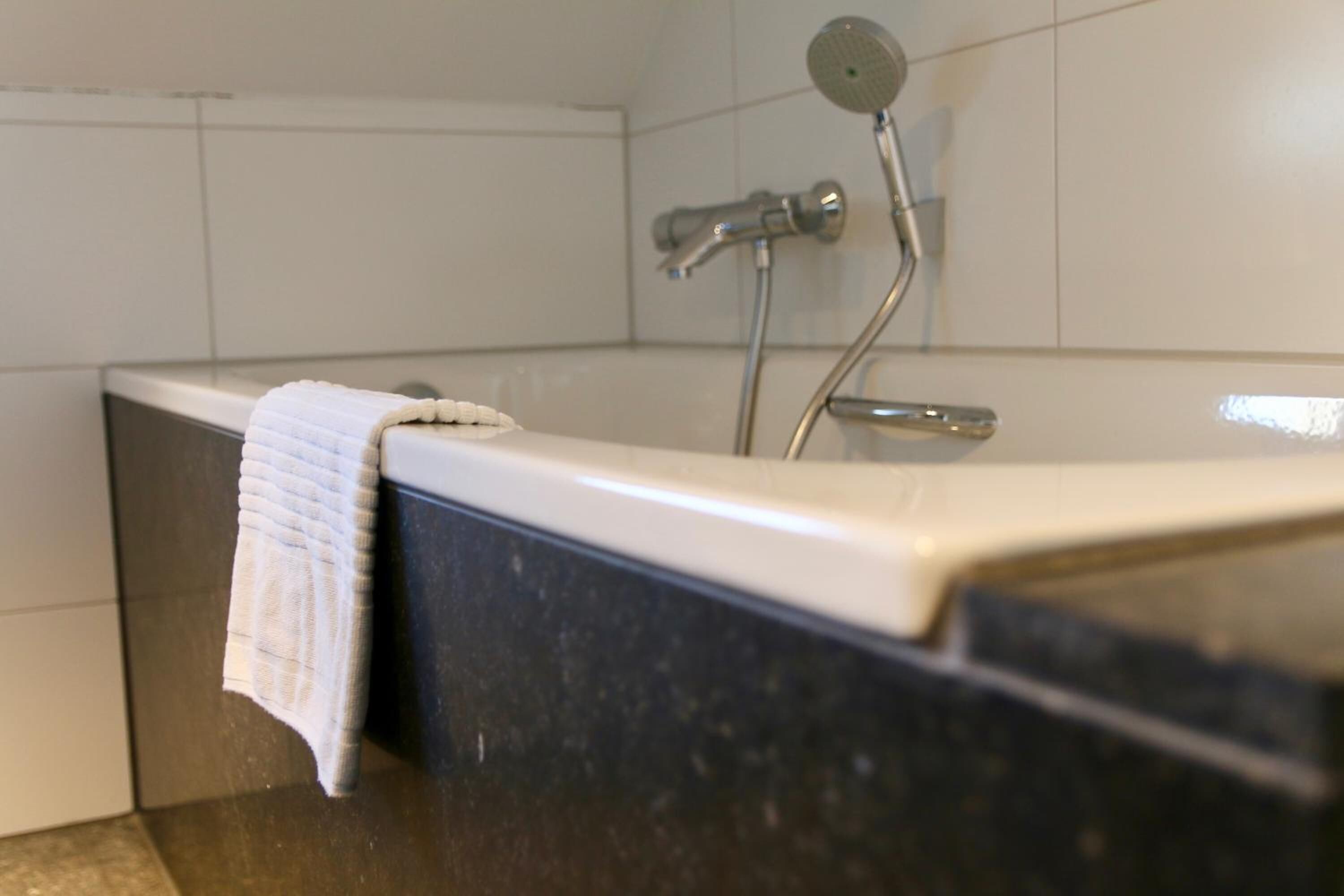 Een badkamer met een bad, een douchekop en een handdoek aan de zijkant.