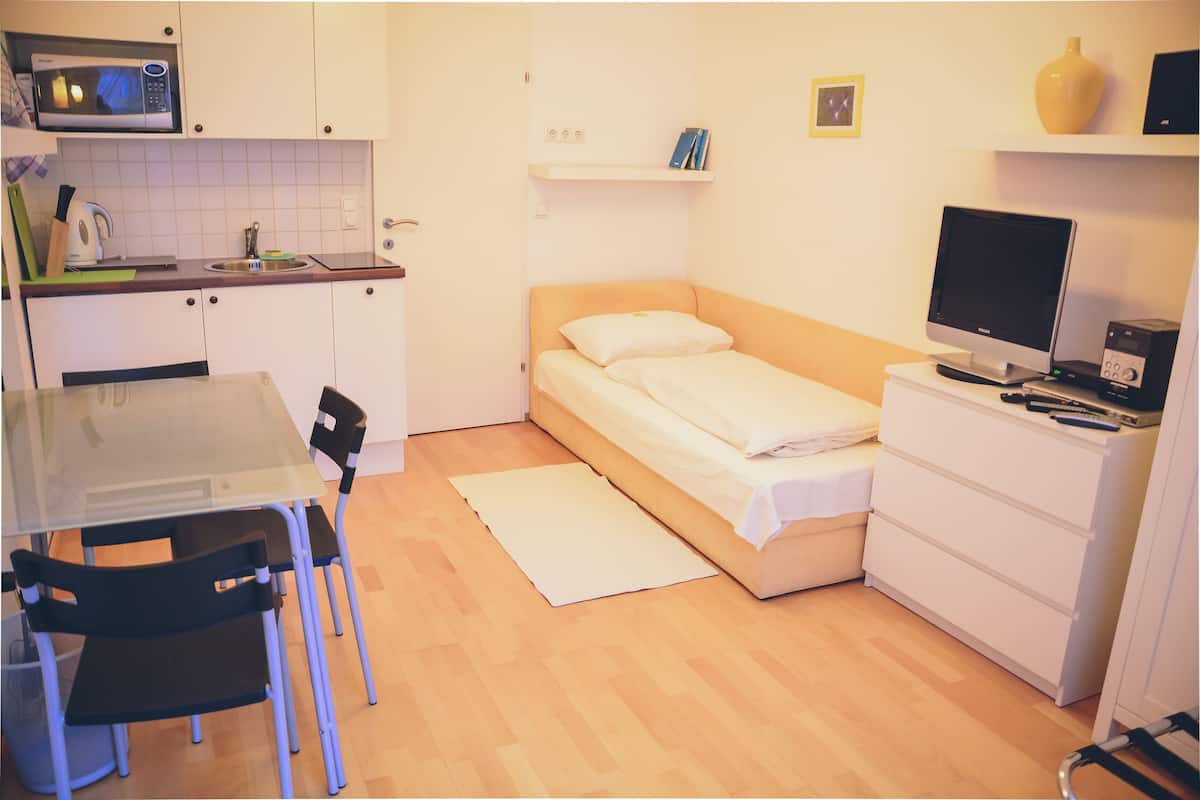 Une petite pièce comprenant un coin cuisine, un lit, un bureau et un ordinateur.