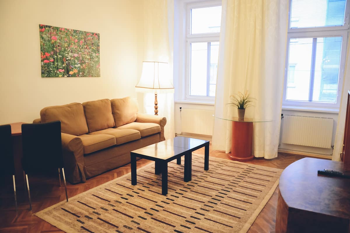 Un salon avec un canapé marron, une table basse, une lampe, une plante en pot et une fenêtre avec des rideaux.