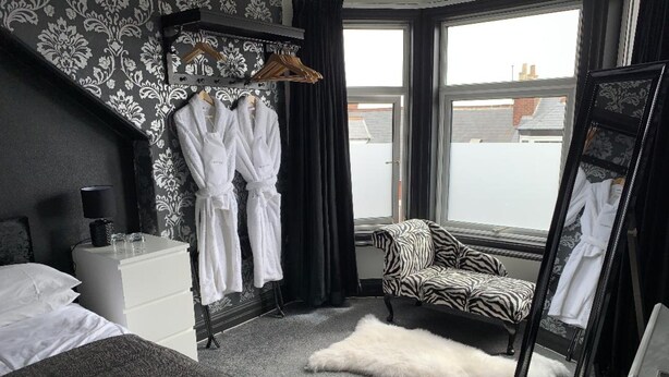 A hotel room with a bed, a dresser, a zebra-patterned chair, a white fur rug, and a window with a view of buildings. - Kingsmere Guest House (South Shields)
