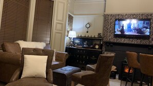 A living room with a fireplace, a television mounted on the wall, and a vintage record player. - Kingsmere Guest House (South Shields)