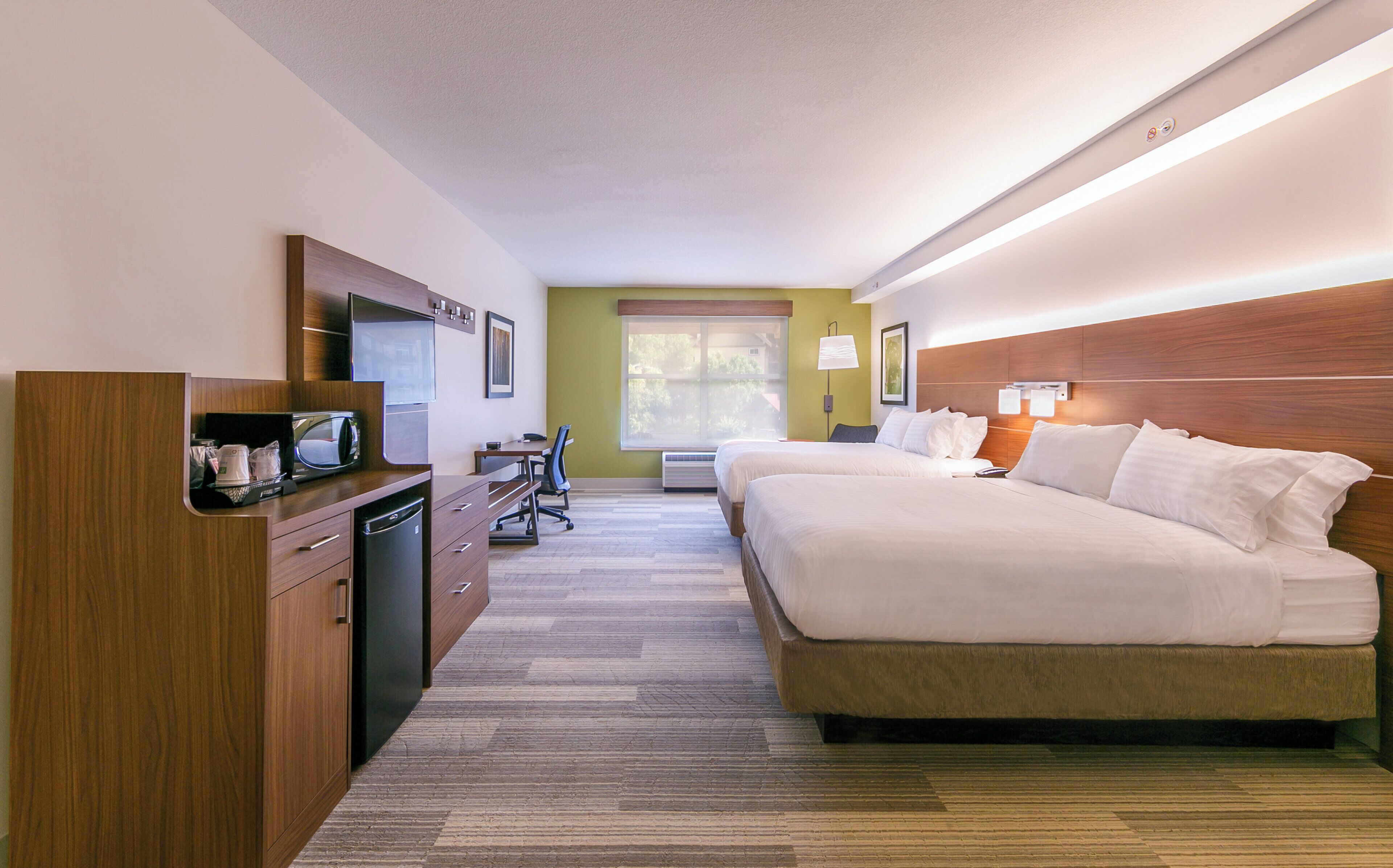 A hotel room with a bed, a desk, a chair, a microwave, and a refrigerator.